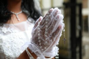 First Communion child's hands in prayer with a rosary. 